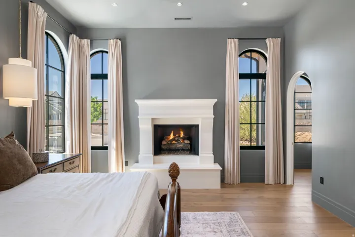 Hardwood flooring featuring an arched entryway, a built-in fireplace with a white mantel, and arched windows
