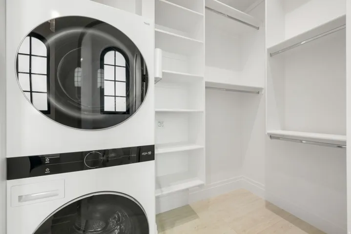 Stacked washer and dryer unit, built-in shelving, multiple hanging rods, and light-toned tile flooring