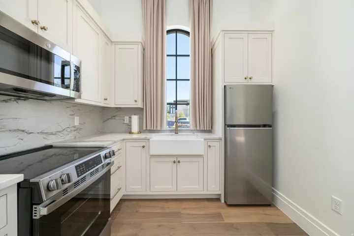Kitchen featuring white cabinetry, stainless steel appliances, a farmhouse sink, and a large arched window