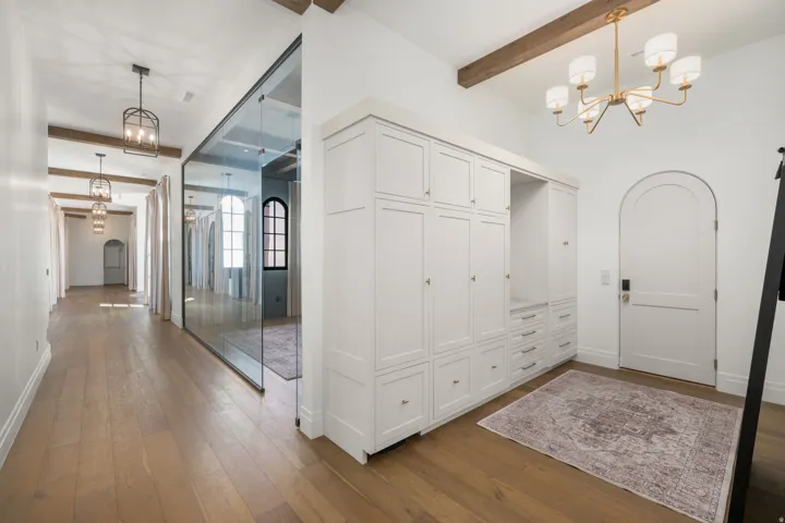 Wide plank wood-finish flooring, exposed ceiling beams, built-in cabinetry, an arched doorway, and contemporary light fixtures