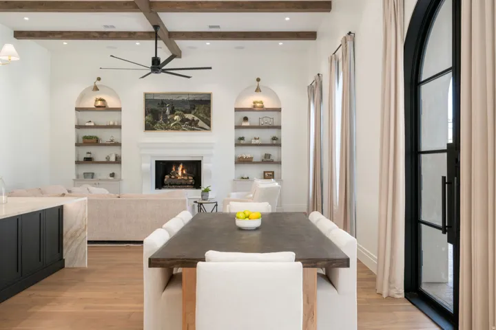 Exposed wood ceiling beams, a decorative fireplace with a mantel, built-in recessed shelving, wood-finish flooring, and an arched glass-panel door