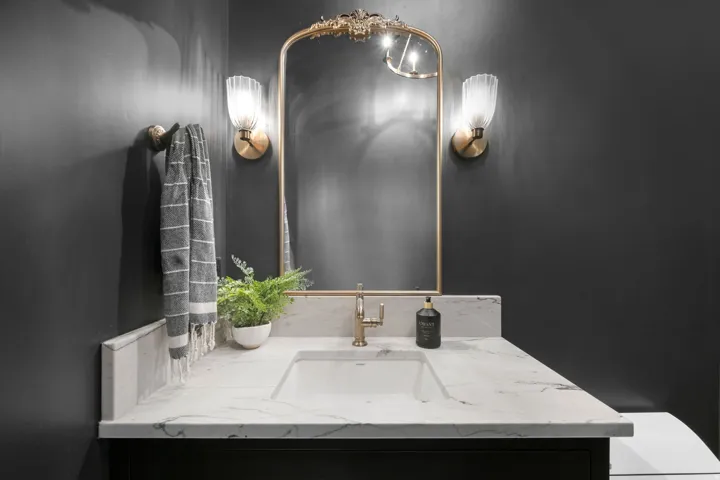 Vanity with an integrated rectangular sink, stone countertop, gold-finish faucet, framed mirror, and wall-mounted sconces