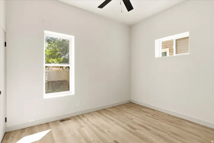 Light-filled room featuring wood-finish flooring, white walls, multiple windows, and a ceiling fan