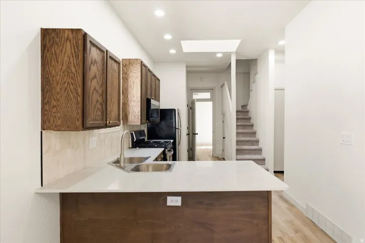Kitchen featuring a dual basin sink, white countertop, dark wood-finish cabinetry, and black appliances