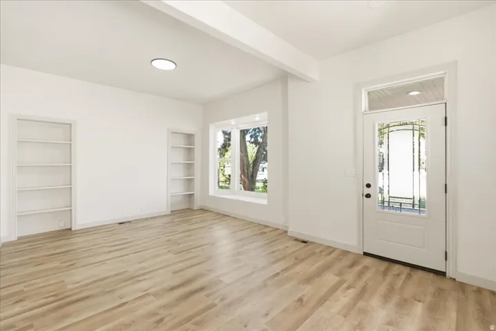 Entry with a decorative glass panel door and transom window, light wood-finish flooring, built-in shelving, a bay window, and a flush-mount ceiling light fixture