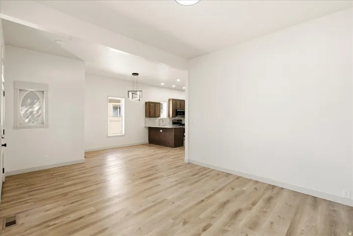 Spacious interior with wood-finish flooring, white walls, recessed lighting, and a contemporary pendant light fixture