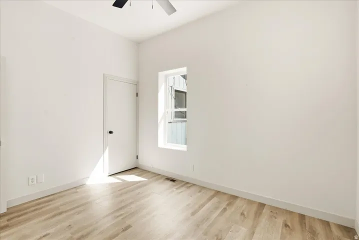 Wood-finish flooring, white walls, ceiling fan, and a single window