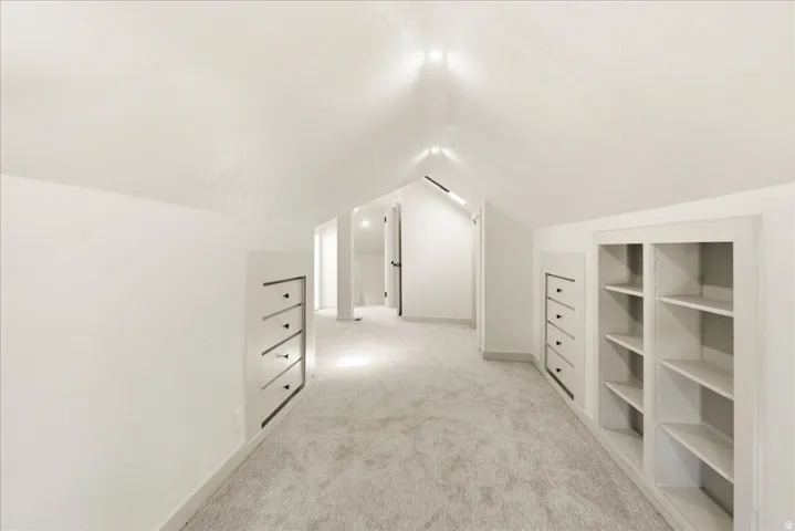 Vaulted ceiling with recessed lighting, light-toned carpeting, built-in shelving, and integrated drawer storage