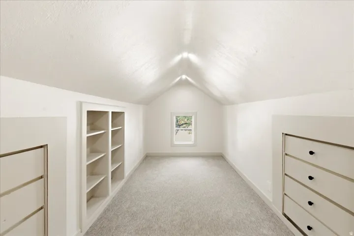 Vaulted ceiling, built-in shelving, built-in drawer storage, window, and grey carpeting