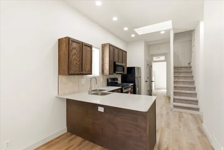 Kitchen with wood-finish cabinetry, light-toned countertops, and stainless steel sink