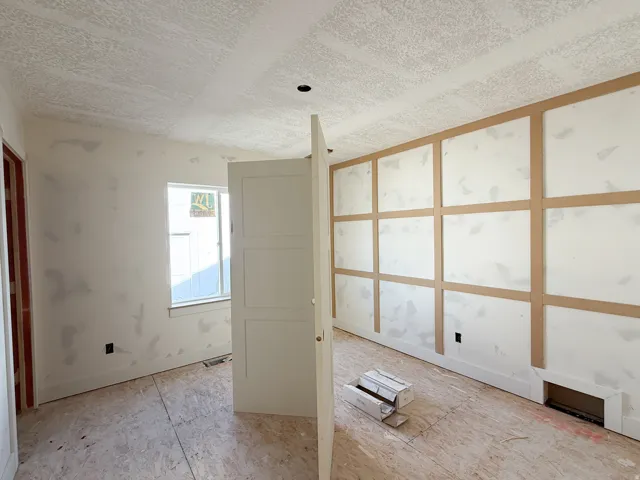 Three-panel interior door, window with trim, decorative wall paneling, and a floor register