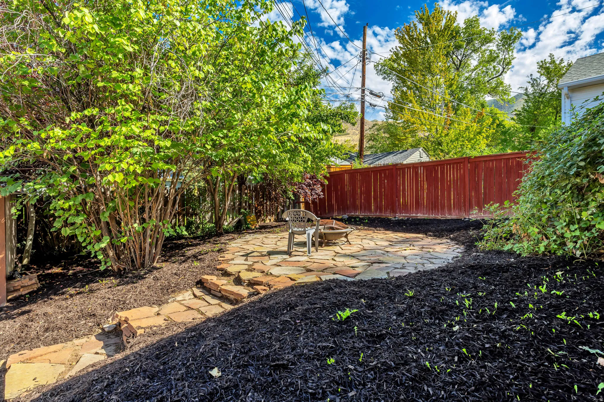Flagstone patio with a built-in fire pit, surrounded by lush mature shrubbery