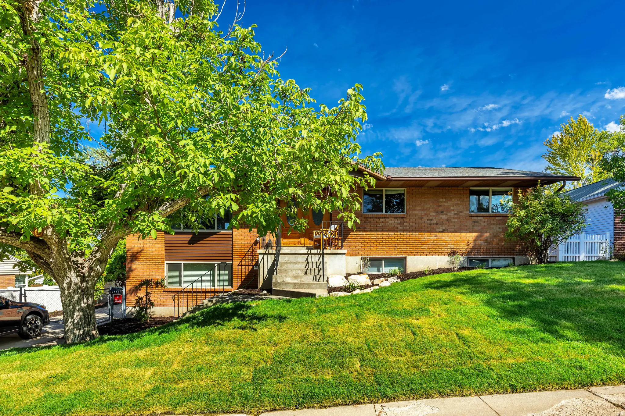 Brick exterior with a prominent front entrance, mature trees, and a sloped front lawn