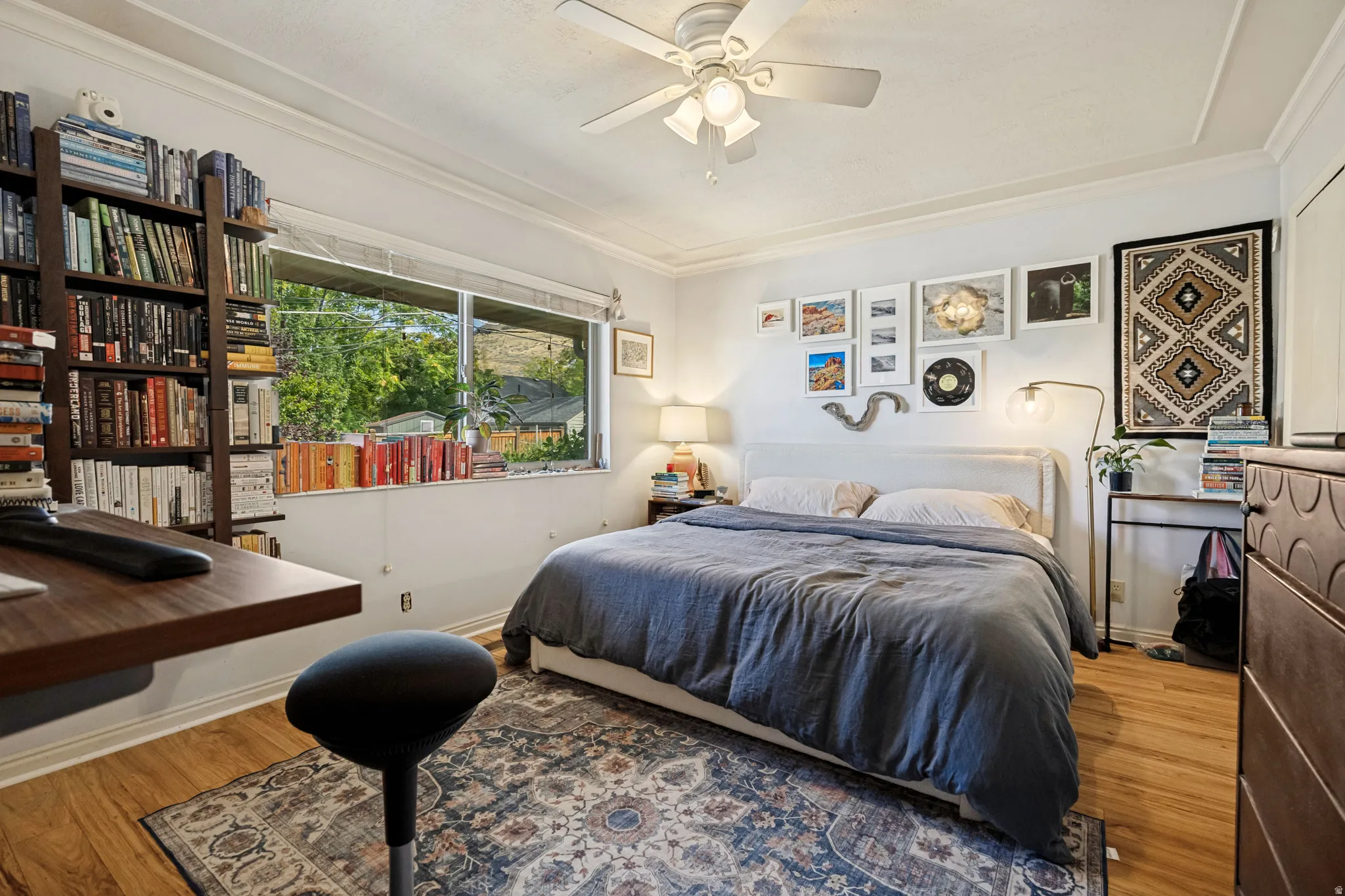 Wood-finish flooring, a contemporary ceiling fan, built-in shelving, a wide window, and crown molding