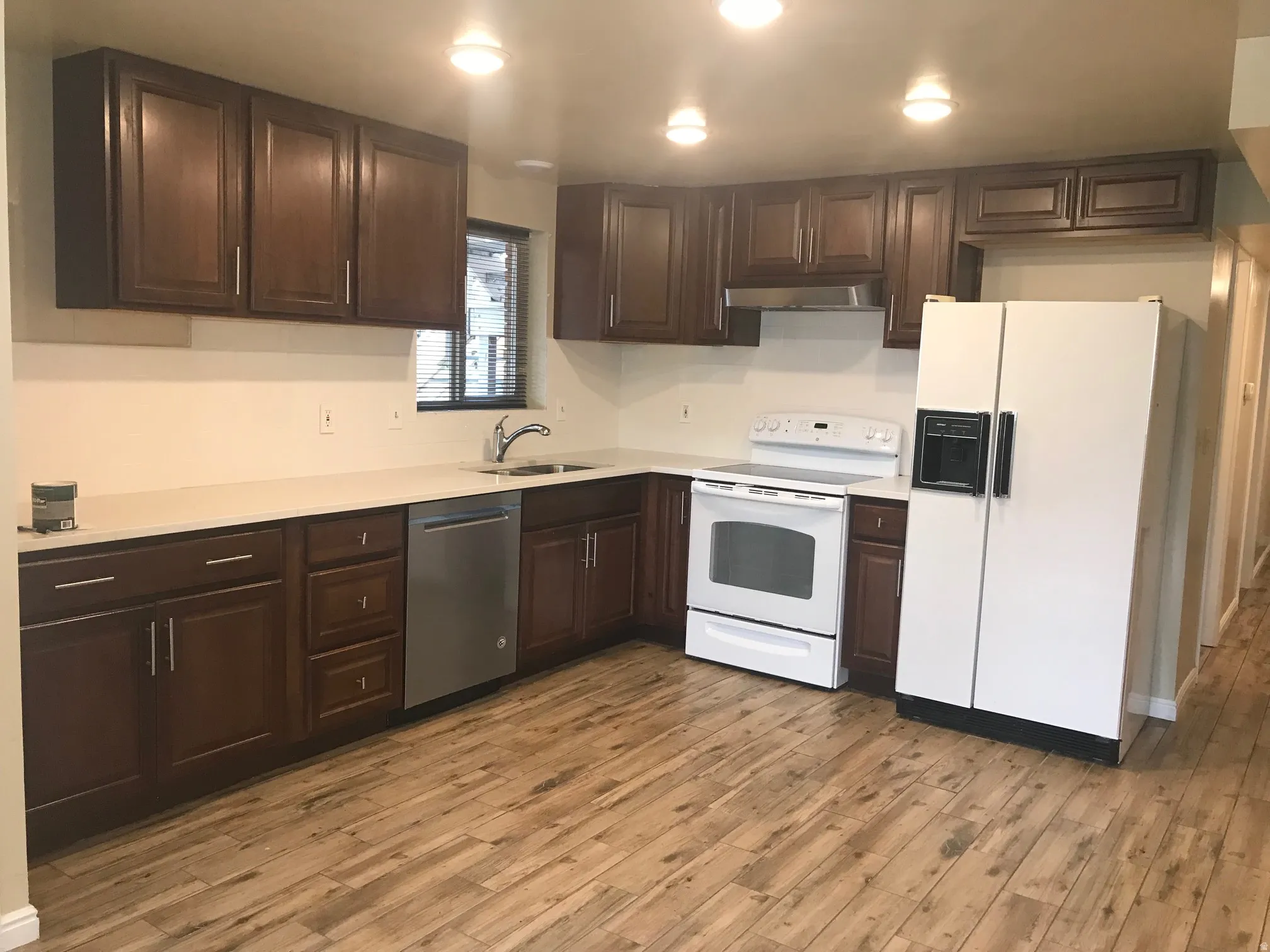 Kitchen featuring wood-finish flooring, dark wood cabinetry, light-toned countertops, a stainless steel dishwasher, and recessed lighting