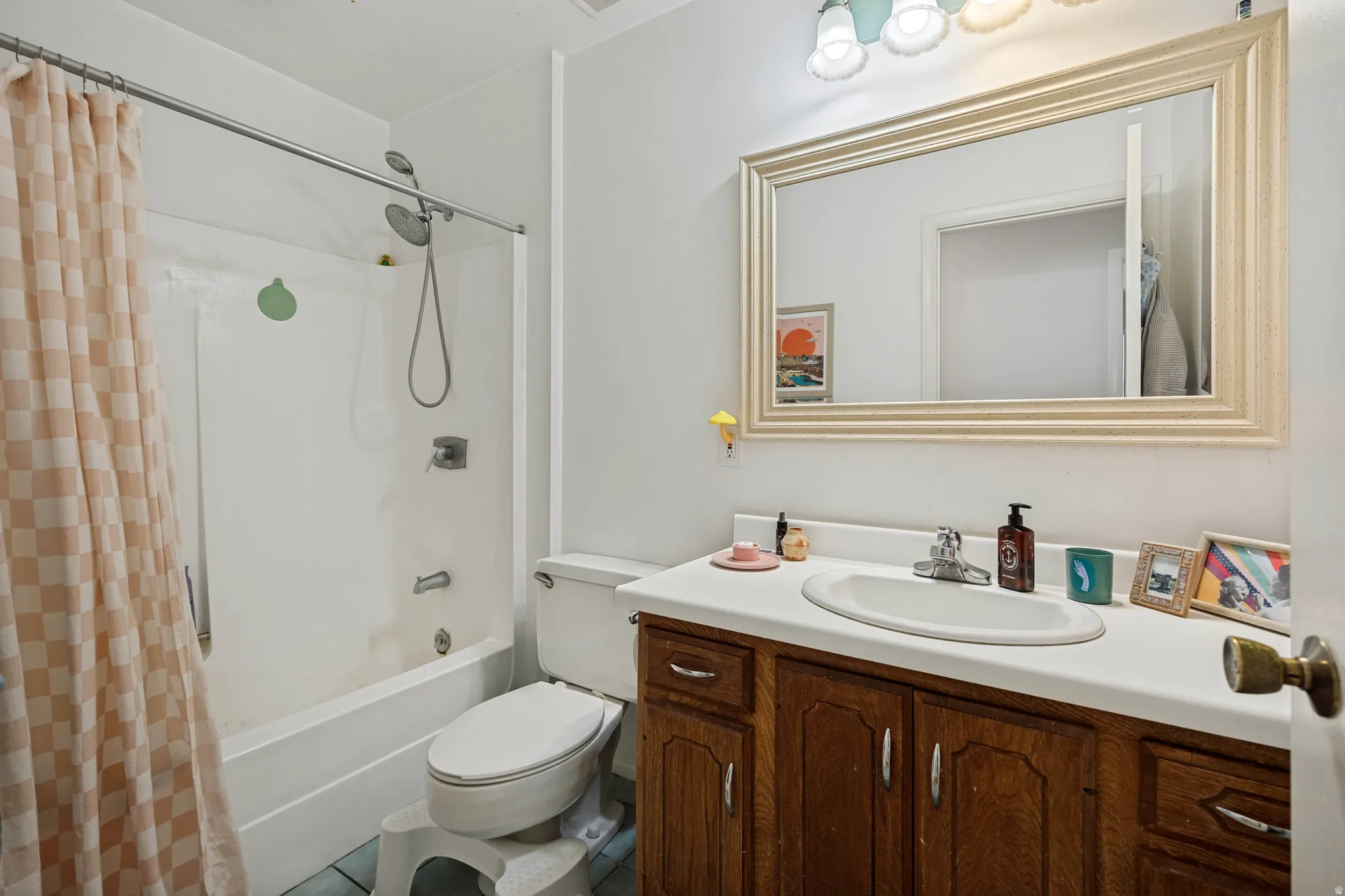 Bathroom featuring a white bathtub with an integrated shower, wood-finish vanity with a white countertop, an oval undermount sink, a framed mirror, and a three-light vanity fixture