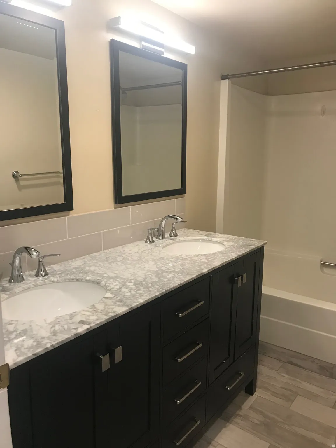 Dual vanity with under-mount sinks, light-toned stone countertop, dark cabinetry with brushed nickel hardware, and a tiled backsplash