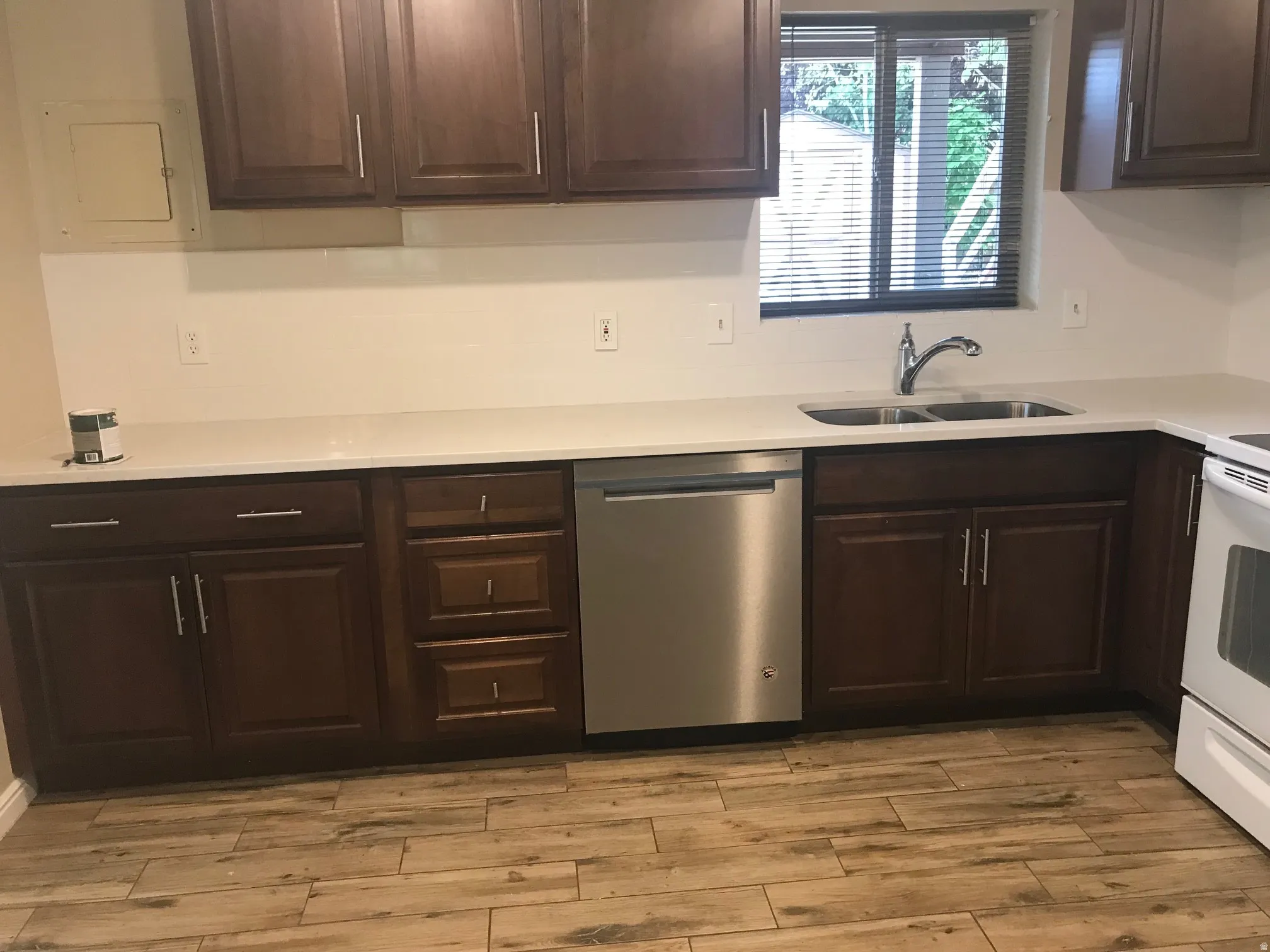 Wood-finish flooring, dark wood cabinetry, light-toned countertops, stainless steel dishwasher, and a double basin sink