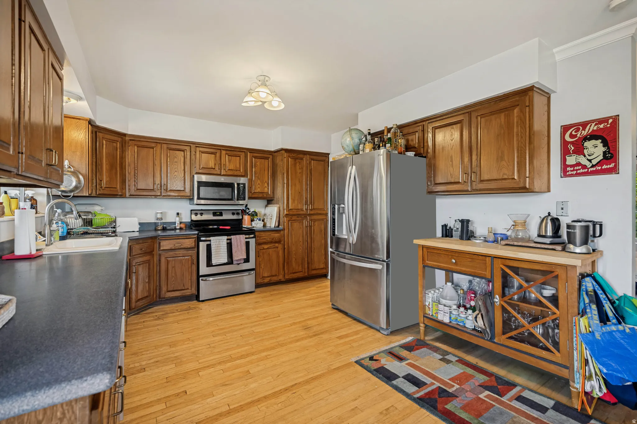 Wood-finish flooring, abundant wood cabinetry, dark countertops, stainless steel appliances, and a built-in kitchen sink