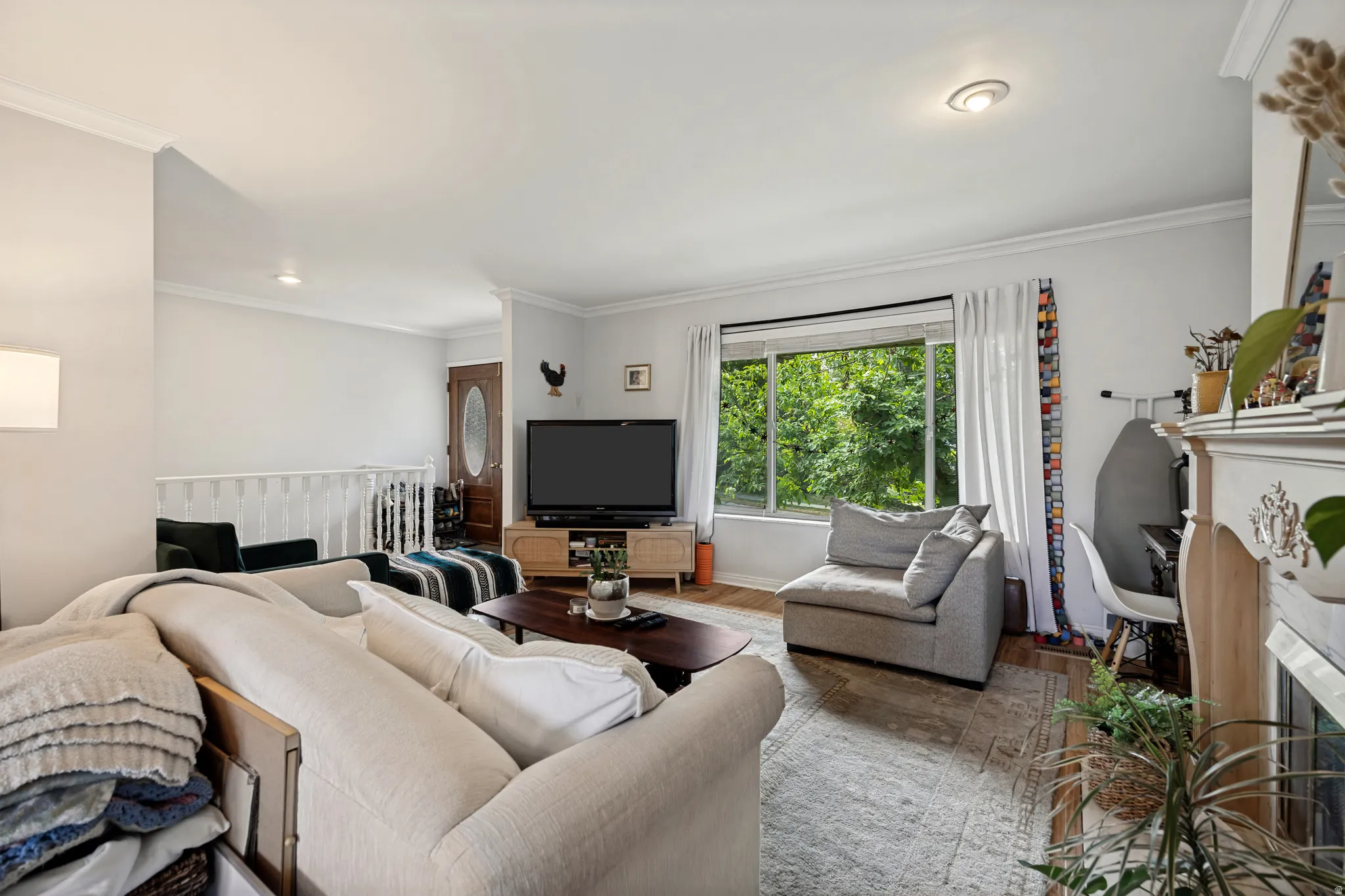 Living area featuring a picture window, crown molding, wood-finish flooring, and a decorative fireplace