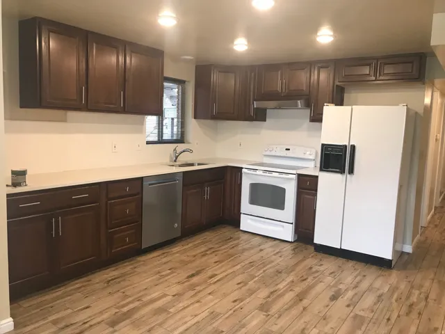 Kitchen featuring wood-finish flooring, dark wood cabinetry, light-toned countertops, a stainless steel dishwasher, and recessed lighting
