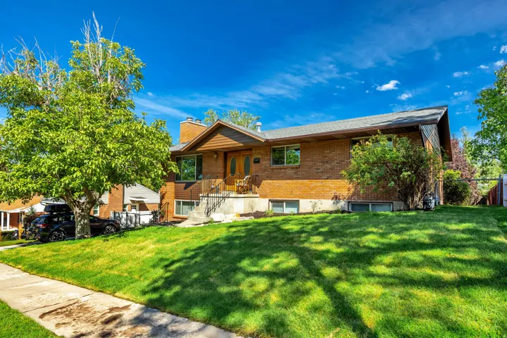 Brick exterior with wood-finish siding accents, a prominent front porch with railings, mature trees, and a sloped front lawn