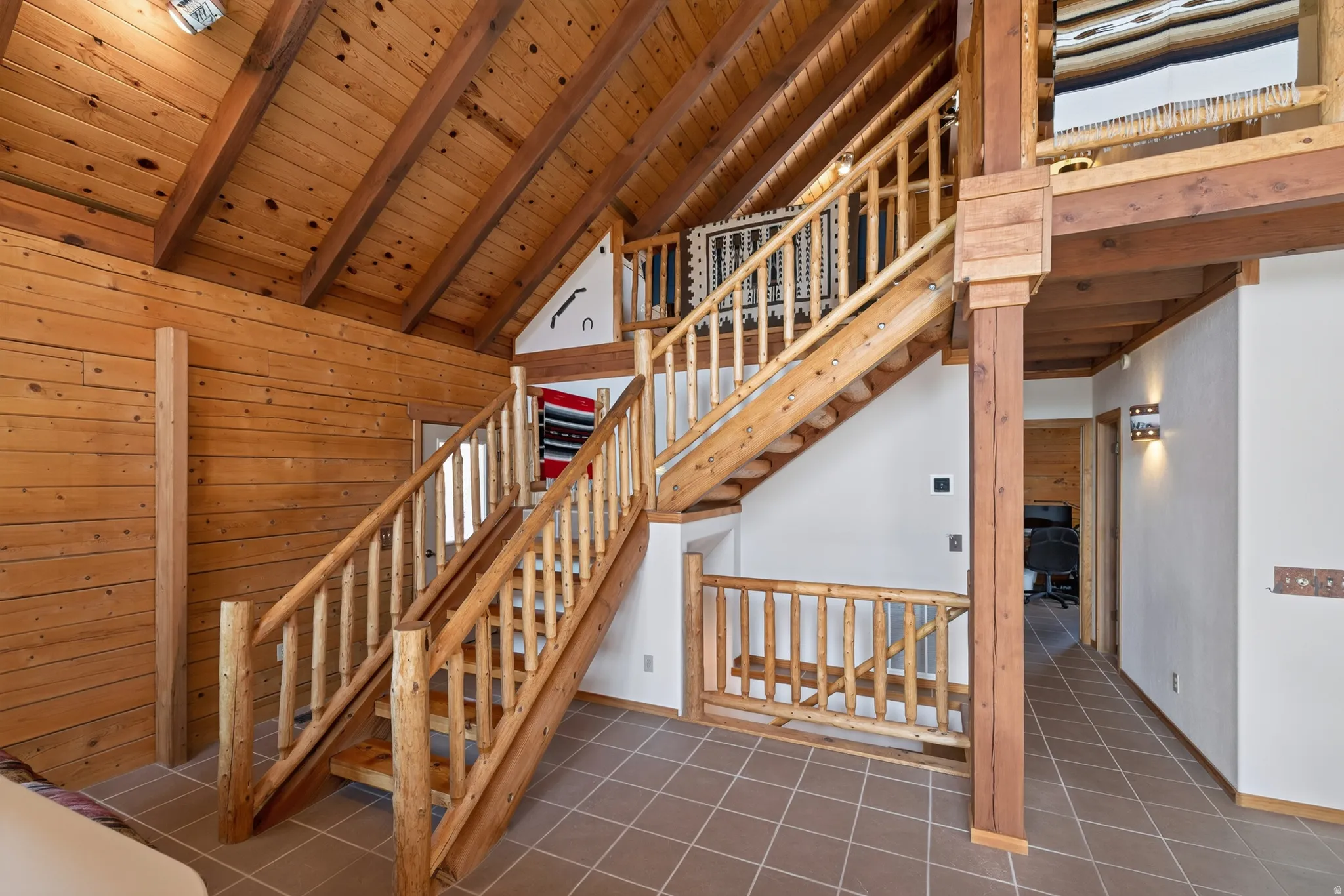 Vaulted wood ceiling, wood-paneled walls, natural wood staircase, wood-finish flooring, and wall sconces