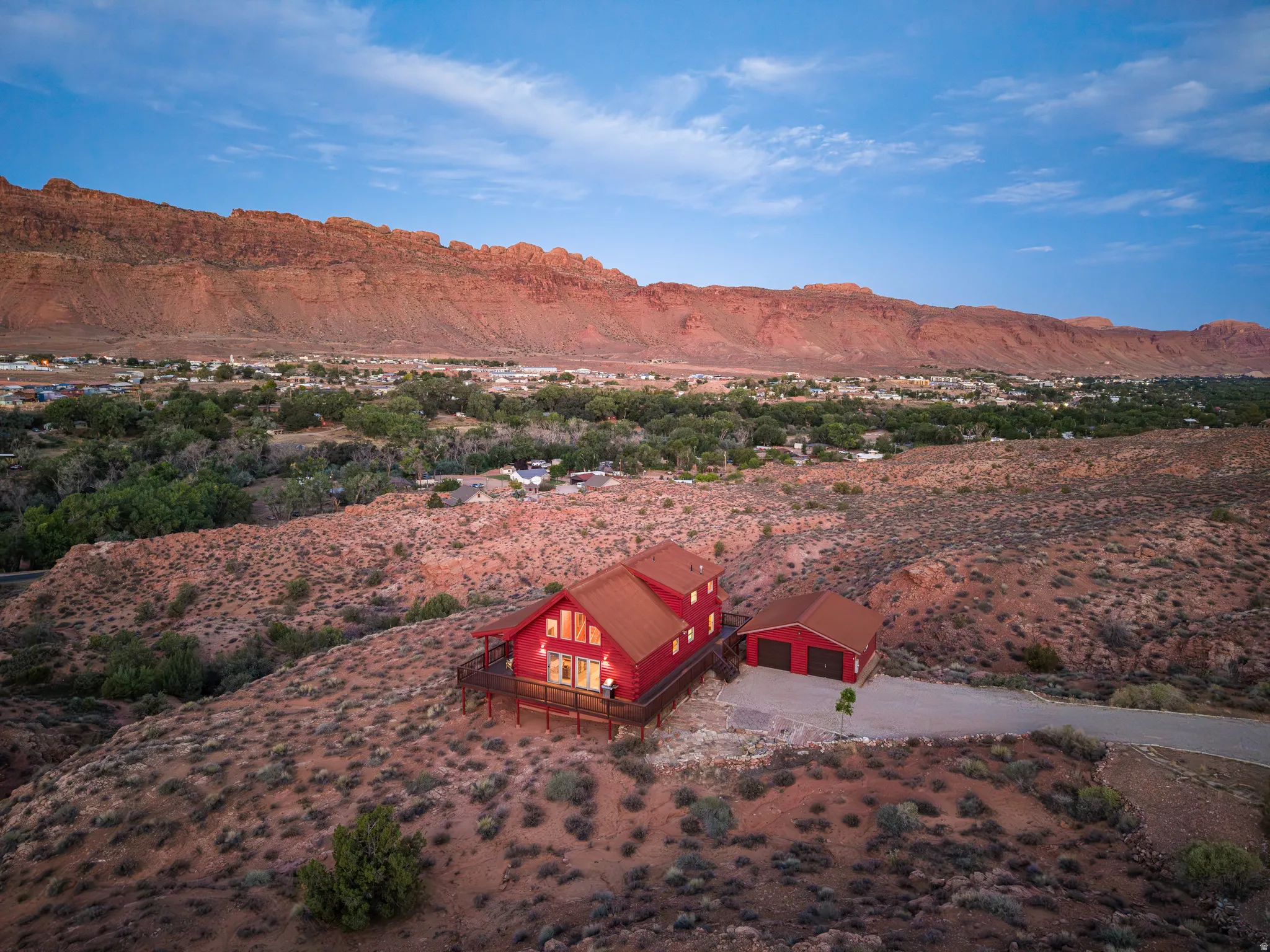 Red exterior with a metal roof, expansive deck, attached garage, and surrounding rugged terrain