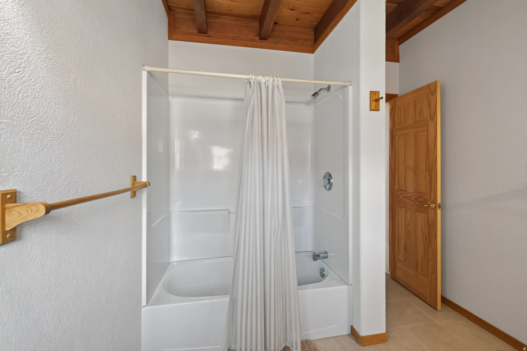Tub/shower combination with chrome fixtures, wood-finish ceiling, and light-toned wall paint