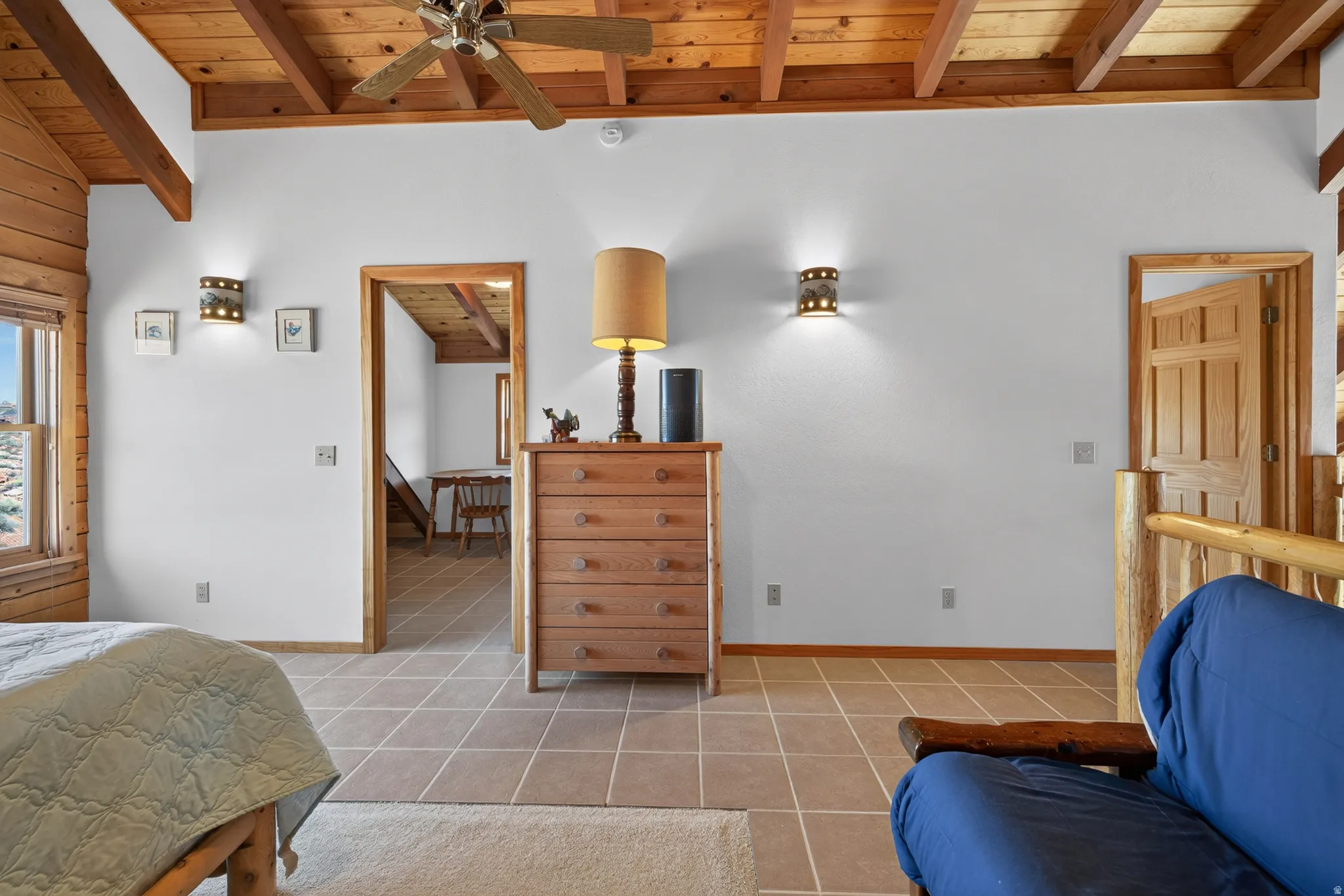 Exposed wood beam ceiling, tile flooring, wood-paneled accent wall, and recessed wall sconces