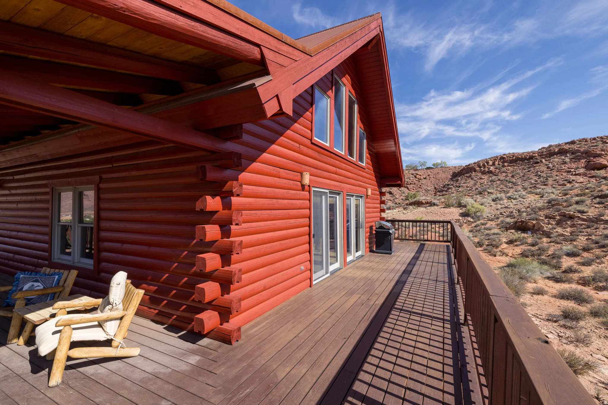 Red log cabin exterior with a pitched roof, a spacious wooden deck with a railing, and multiple glass doors