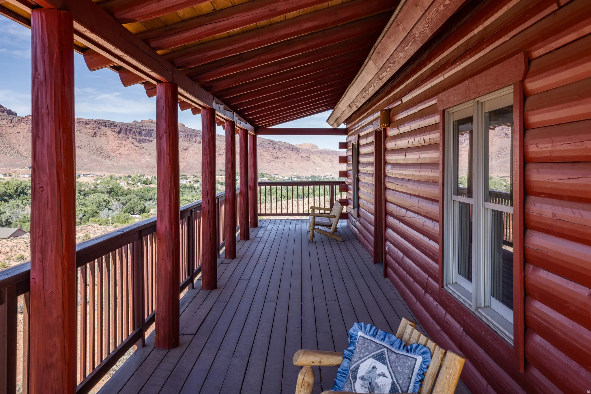 Expansive log cabin-style deck featuring a wood railing, exposed wood ceiling, and multiple windows