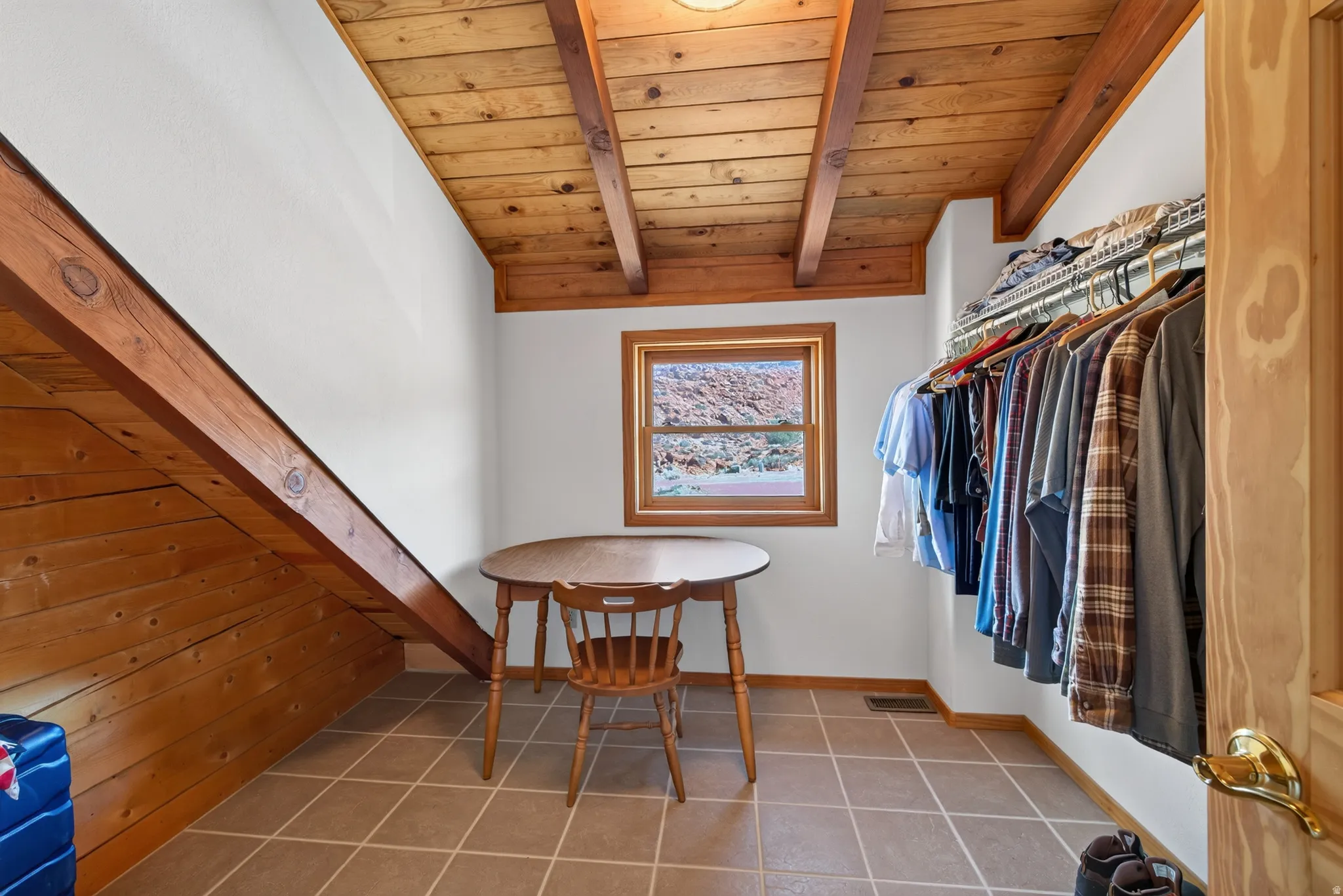 Wood-beamed ceiling, tile flooring, built-in clothing rack, and a wood-framed window