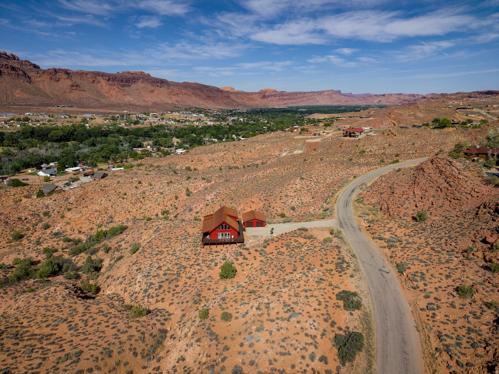 Red-toned home with a contrasting roof and perimeter decking, set on a desert landscape
