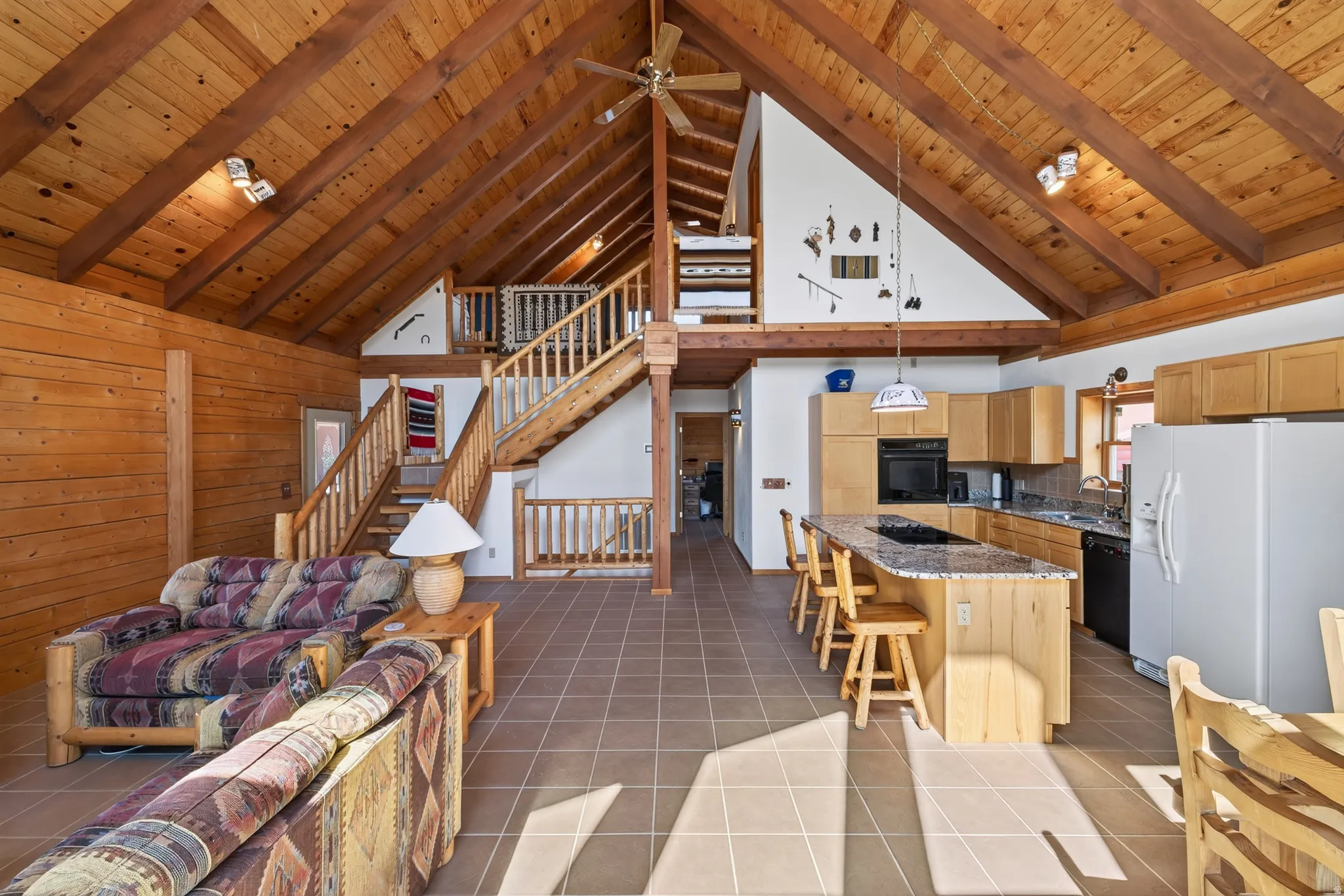 Vaulted wood-paneled ceilings with exposed beams, wood-finish walls, ceramic tile flooring, built-in kitchen cabinetry, and a kitchen island with a stone countertop