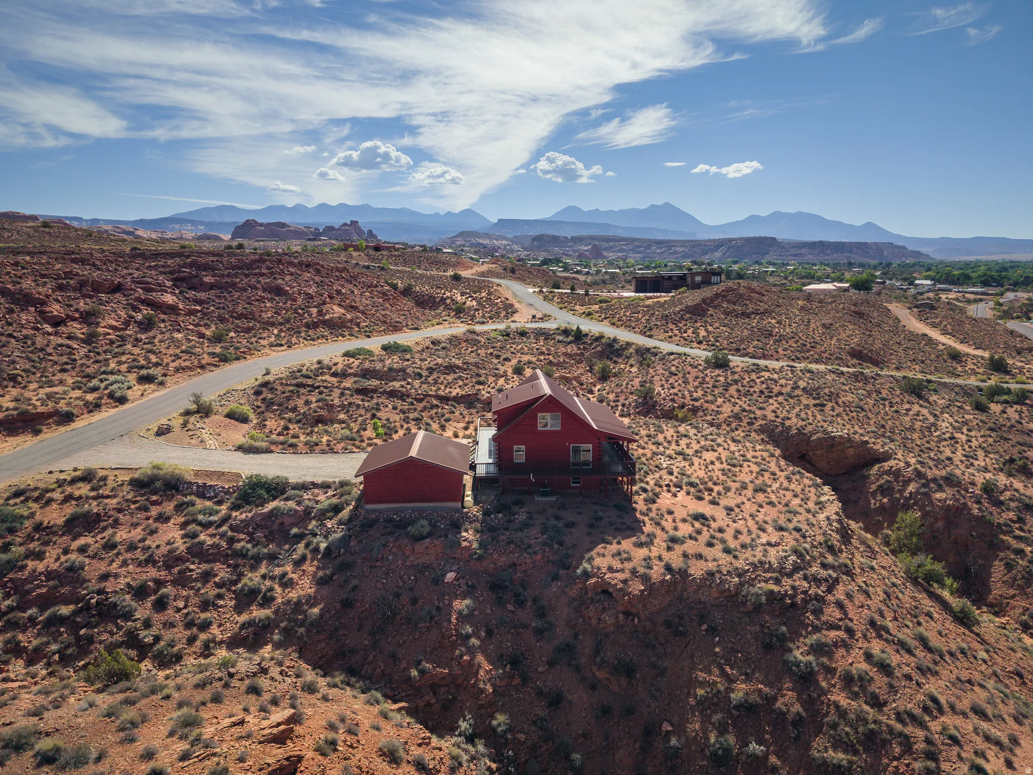 Red-sided house with a dark roof and a separate matching structure, situated on a rocky, elevated landscape