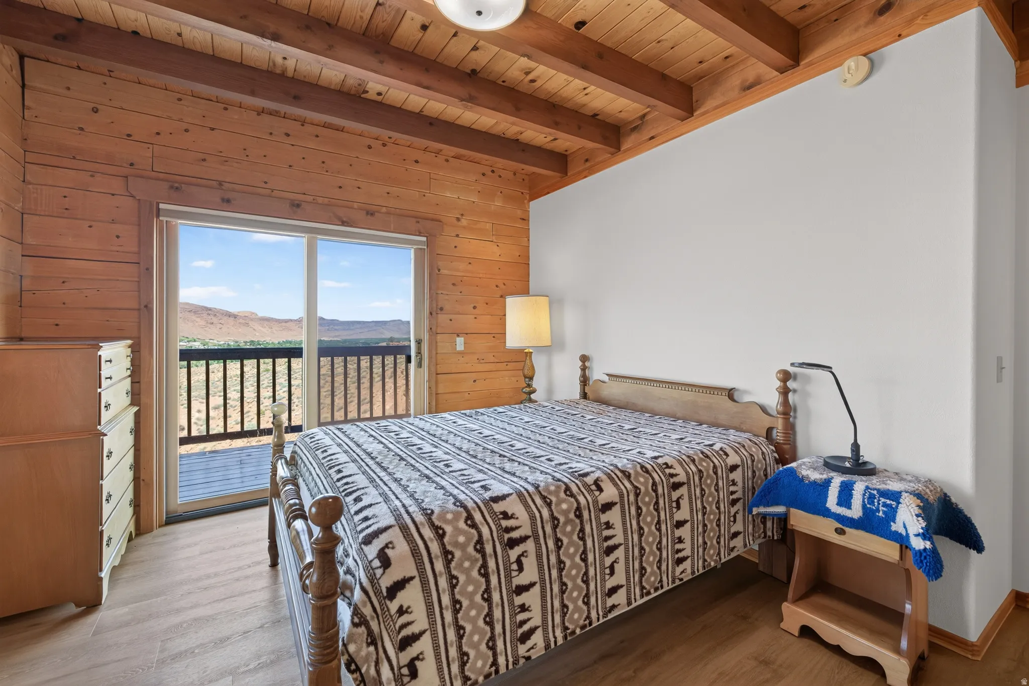 Wood-finish flooring, exposed wood beam ceiling, wood plank wall finish, sliding glass door with balcony, and expansive natural scenery
