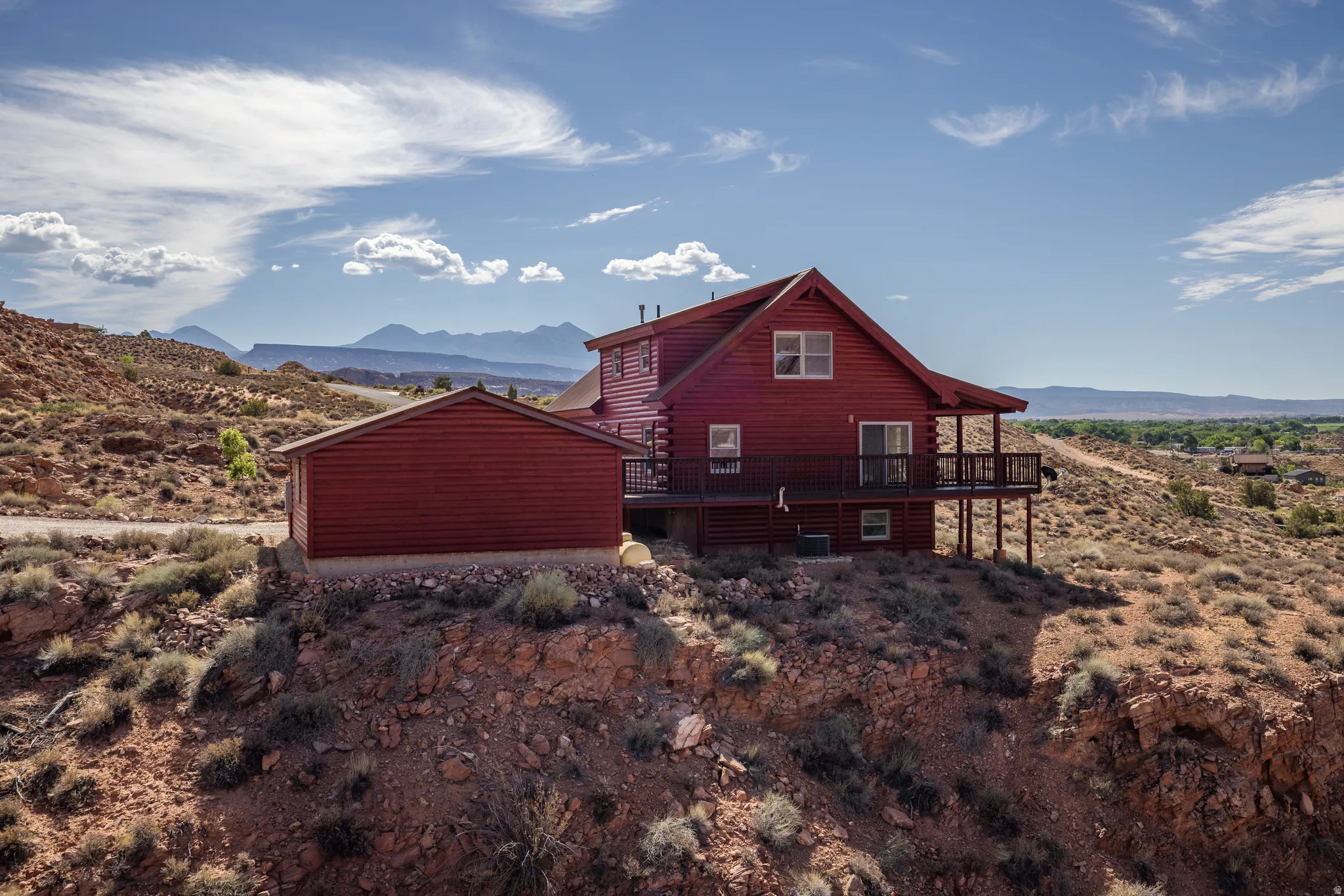 Red-sided dwelling with an attached elevated deck, featuring a gabled roof and surrounding arid landscape