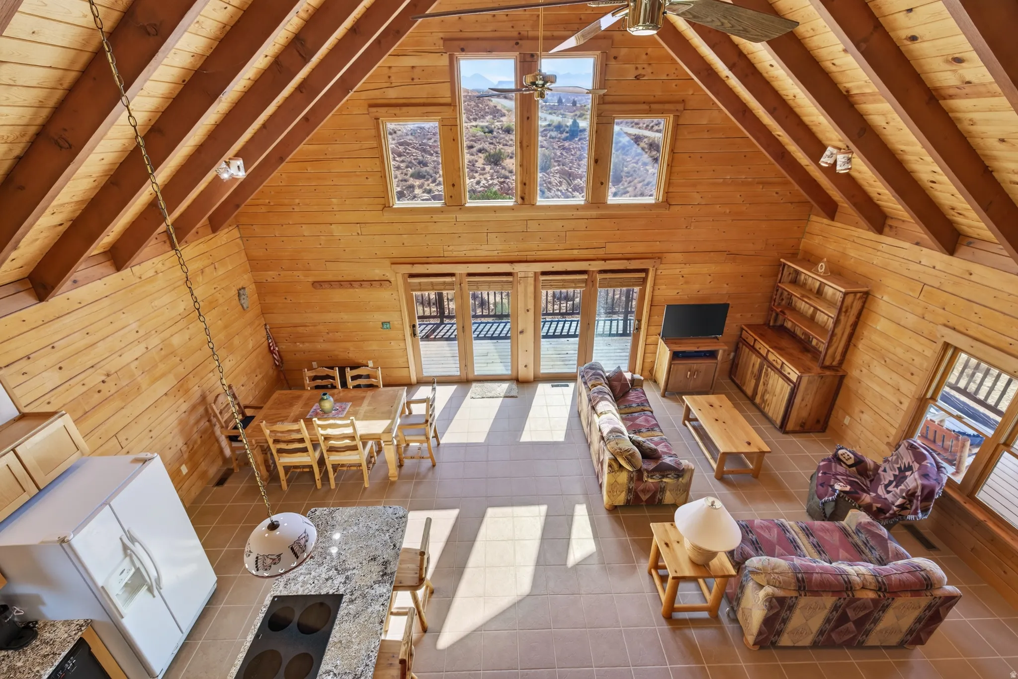 Vaulted ceiling with exposed beams, natural wood paneling, tiled flooring, built-in kitchen island with granite-style countertop, and sliding glass doors