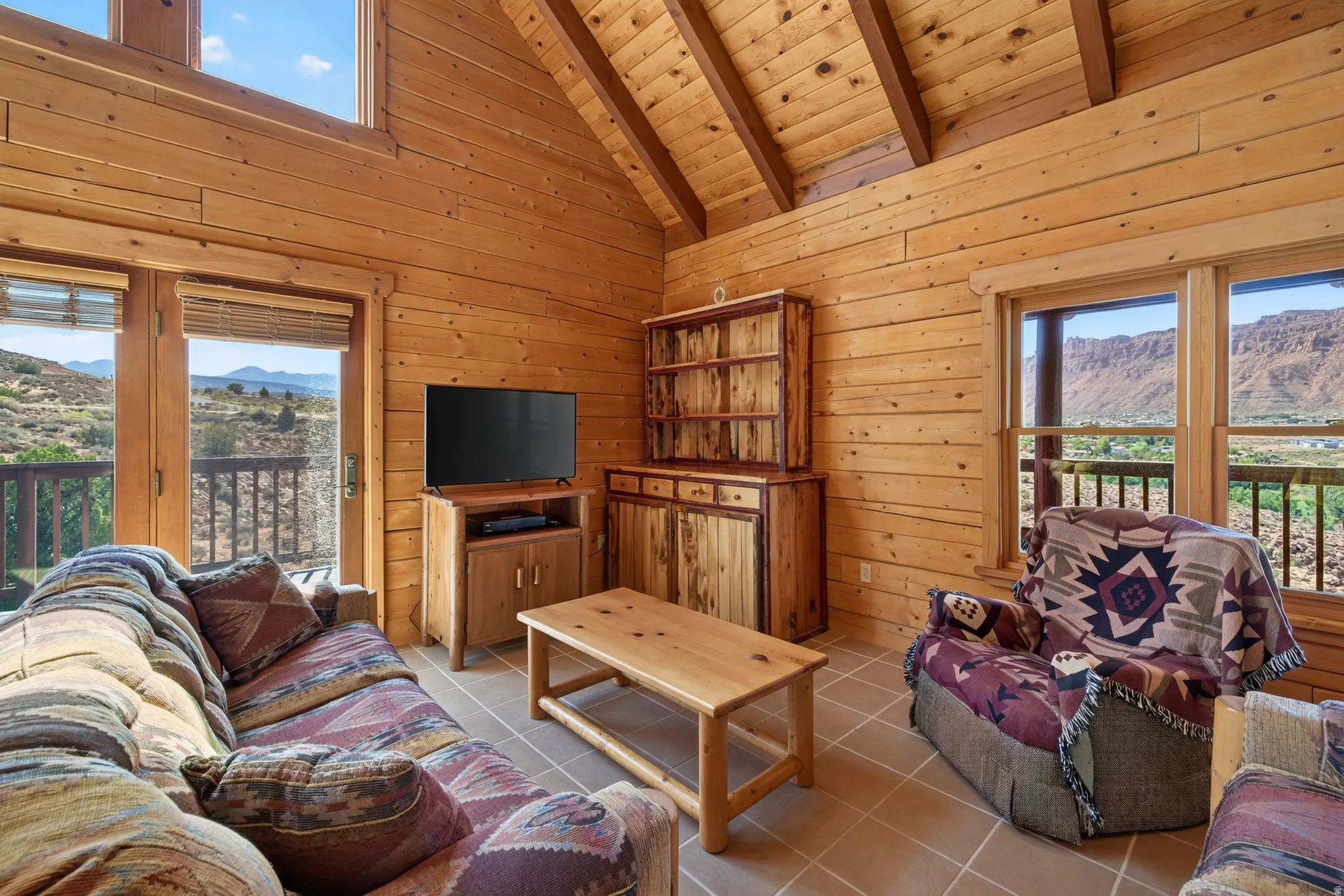 Vaulted wood-paneled ceilings with exposed beams, wood-paneled walls, tiled flooring, natural wood doors, and multiple windows with outdoor scenery