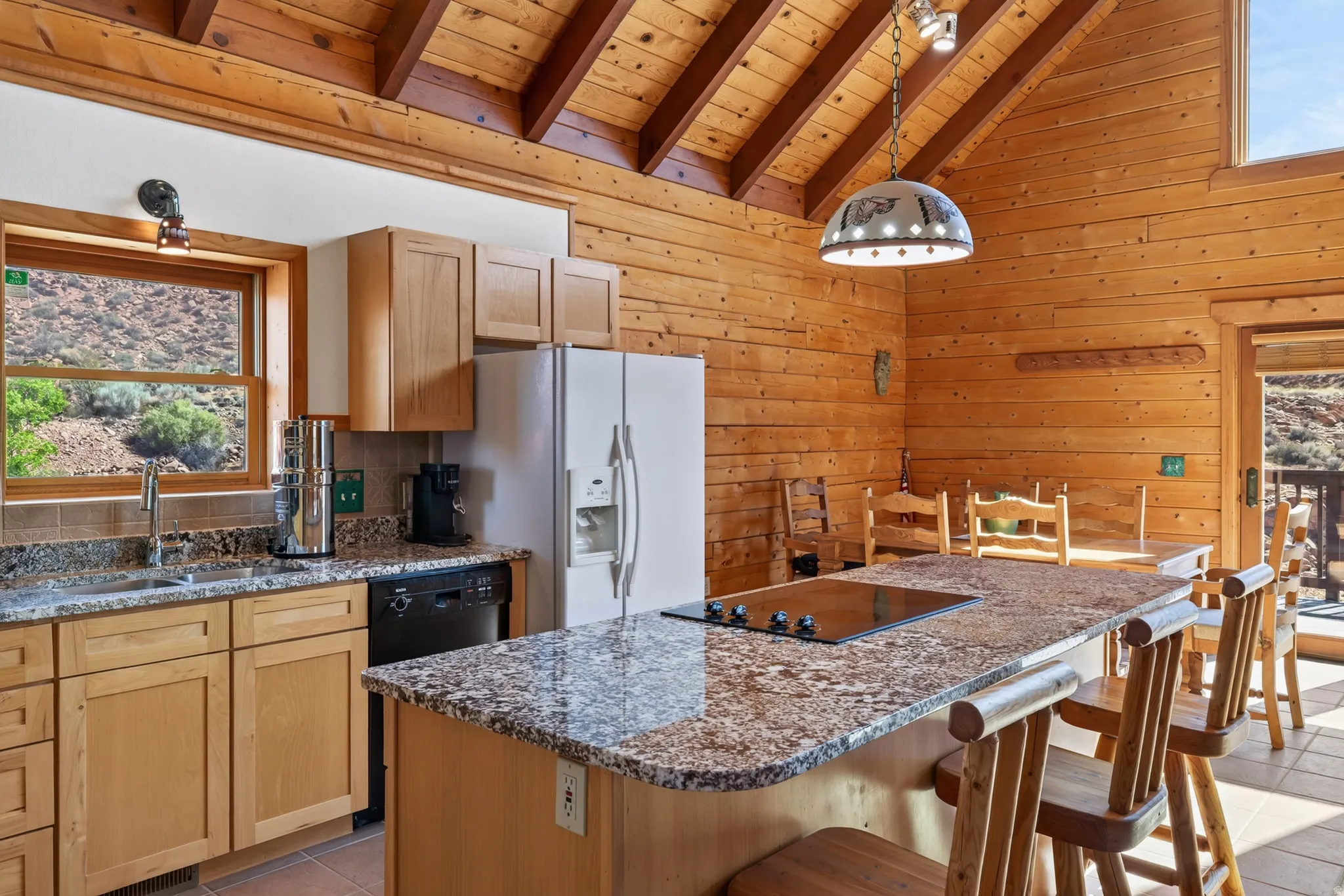 Kitchen featuring wood-paneled walls, vaulted wood-beam ceiling, and an island with a built-in cooktop and granite-style countertop
