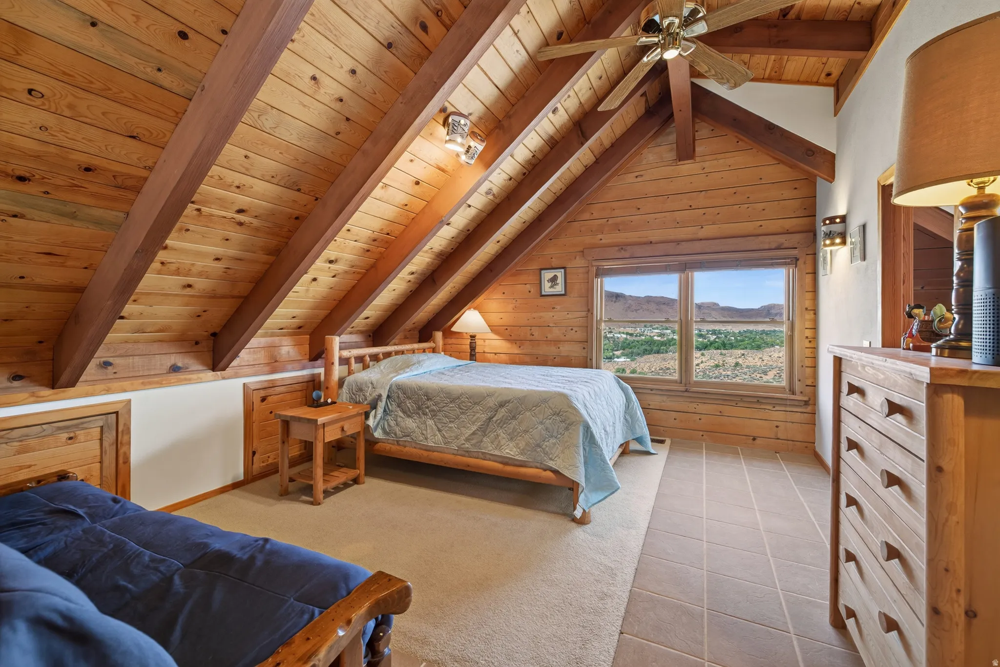 Vaulted wood-paneled ceilings with exposed beams, wood-paneled walls, ceiling fan, carpet and tile flooring, and a window with a mountain backdrop