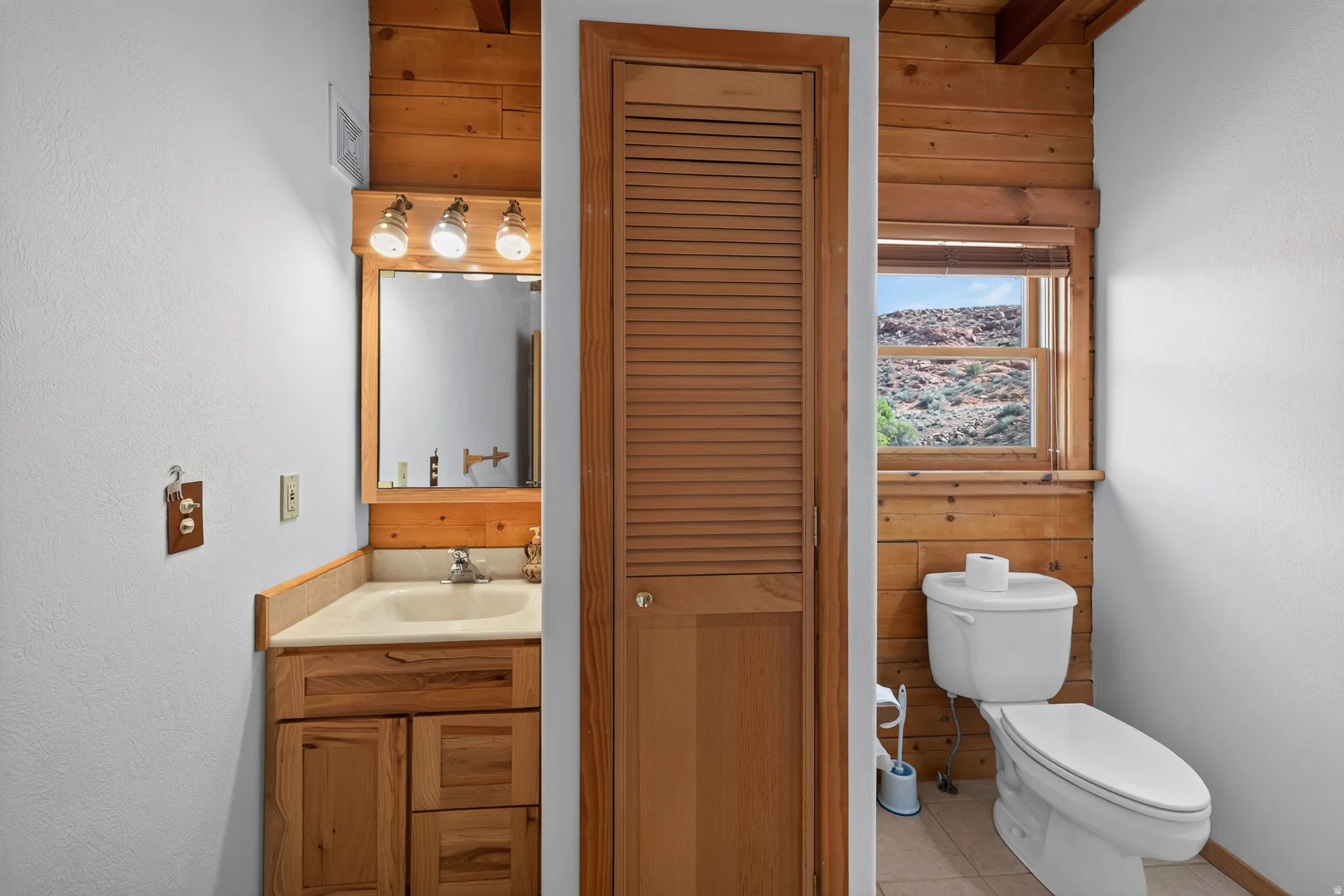 Wood-paneled wall accents, natural wood vanity with integrated sink, wood-framed mirror, and a window offering a natural landscape