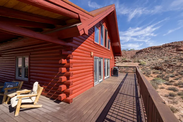 Red log cabin exterior with a pitched roof, a spacious wooden deck with a railing, and multiple glass doors