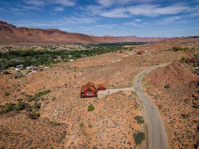 Red-toned home with a contrasting roof and perimeter decking, set on a desert landscape