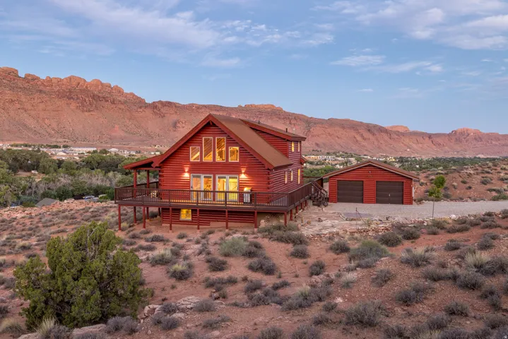 Red-stained log home with a multi-level deck, expansive windows, and a detached two-car garage