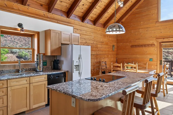 Kitchen featuring wood-paneled walls, vaulted wood-beam ceiling, and an island with a built-in cooktop and granite-style countertop