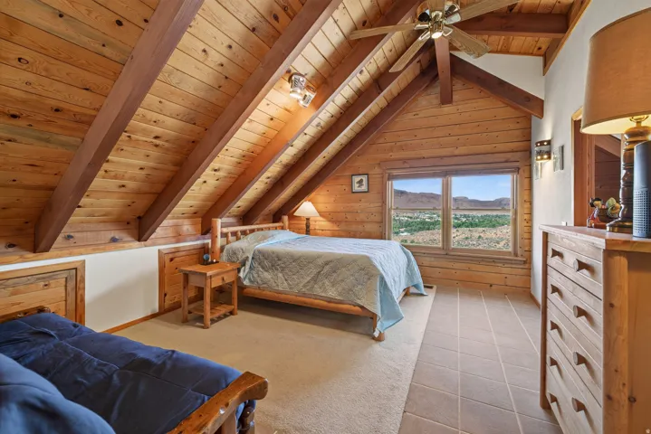 Vaulted wood-paneled ceilings with exposed beams, wood-paneled walls, ceiling fan, carpet and tile flooring, and a window with a mountain backdrop