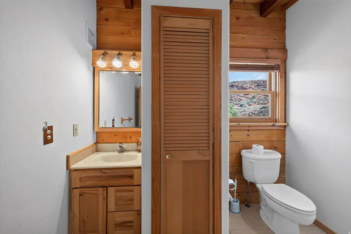 Wood-paneled wall accents, natural wood vanity with integrated sink, wood-framed mirror, and a window offering a natural landscape