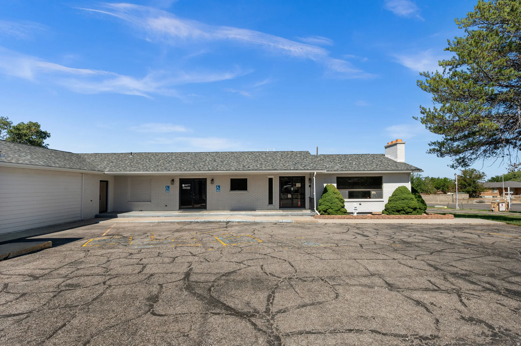 Single-story commercial building with a grey shingle roof, multiple entry points, and a prominent brick chimney feature